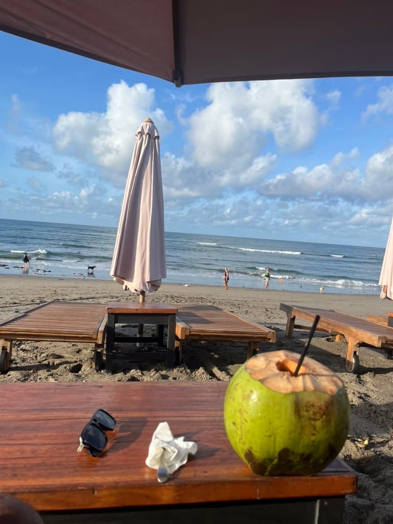 A fresh coconut on a wooden table at a beach club, looking out over the sand and surf in Canggu