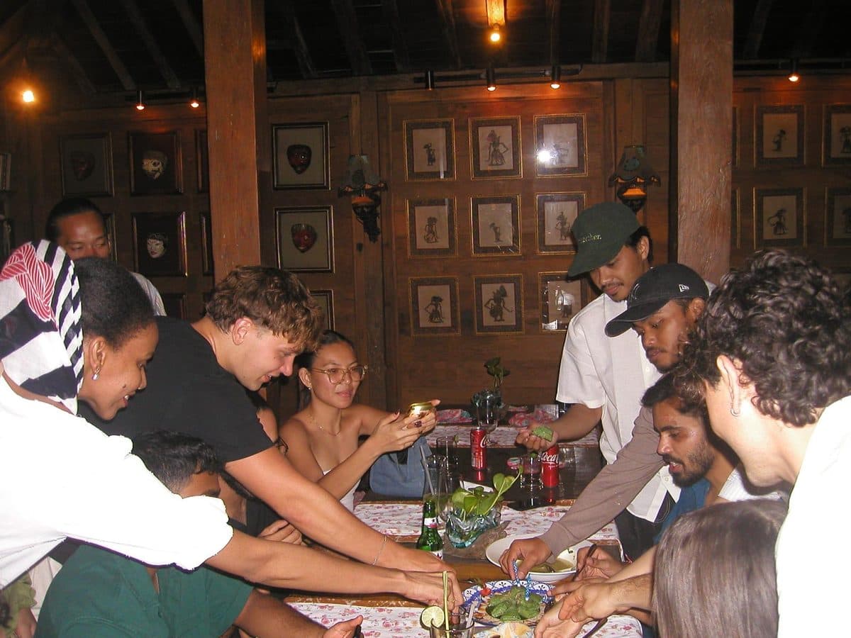 Interns crowding a long table over shared plates at a warung dinner