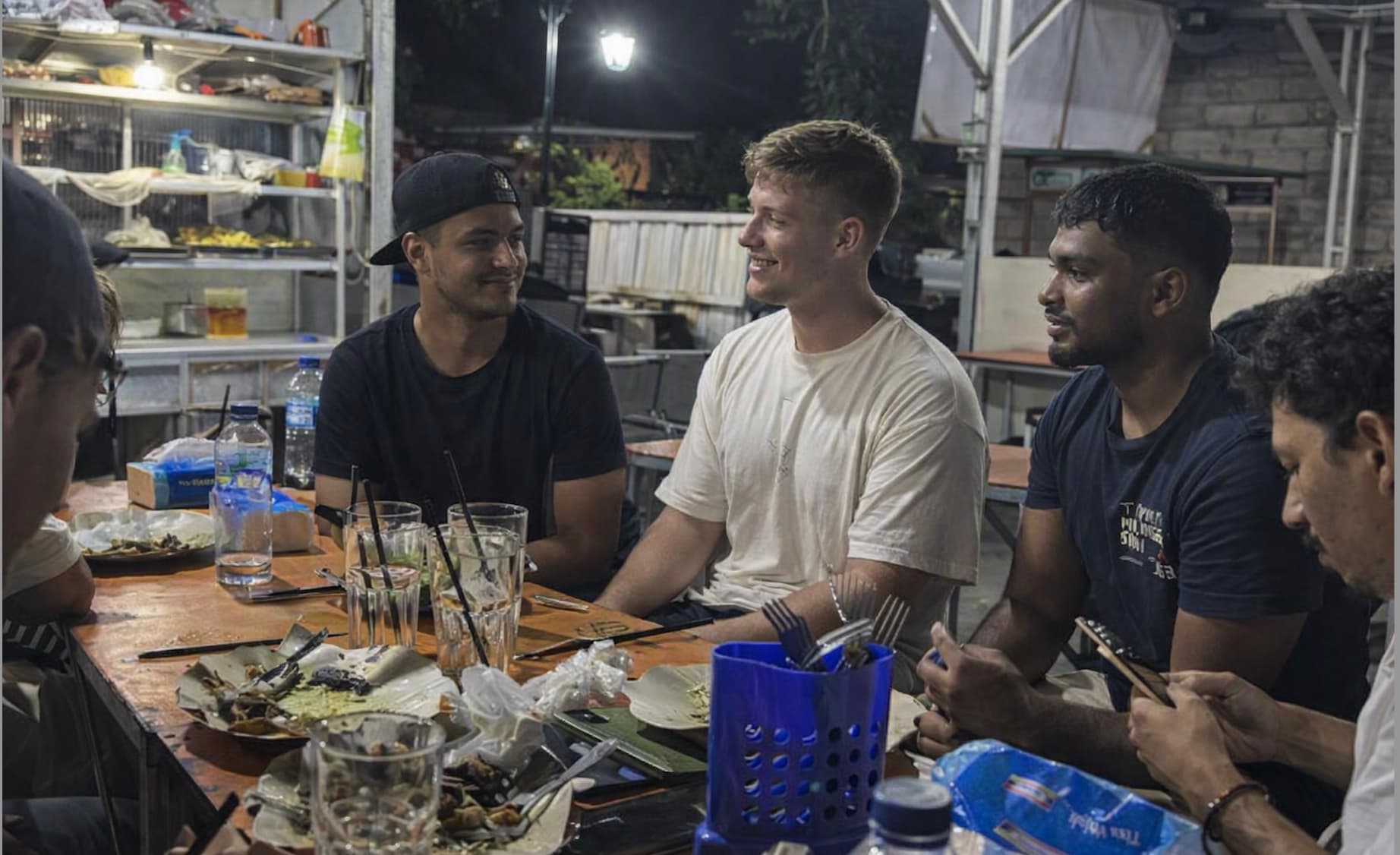 A group of interns eating together at a long table at an outdoor warung in the evening