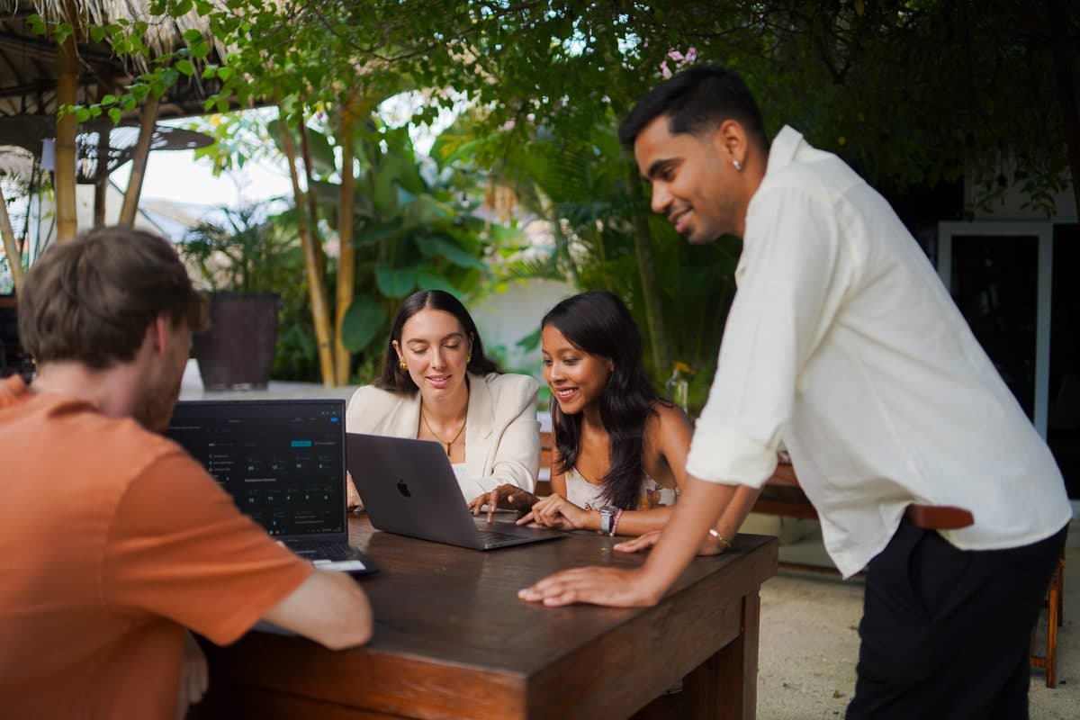 A supervisor leaning over a laptop explaining work to three interns at an outdoor table in Bali