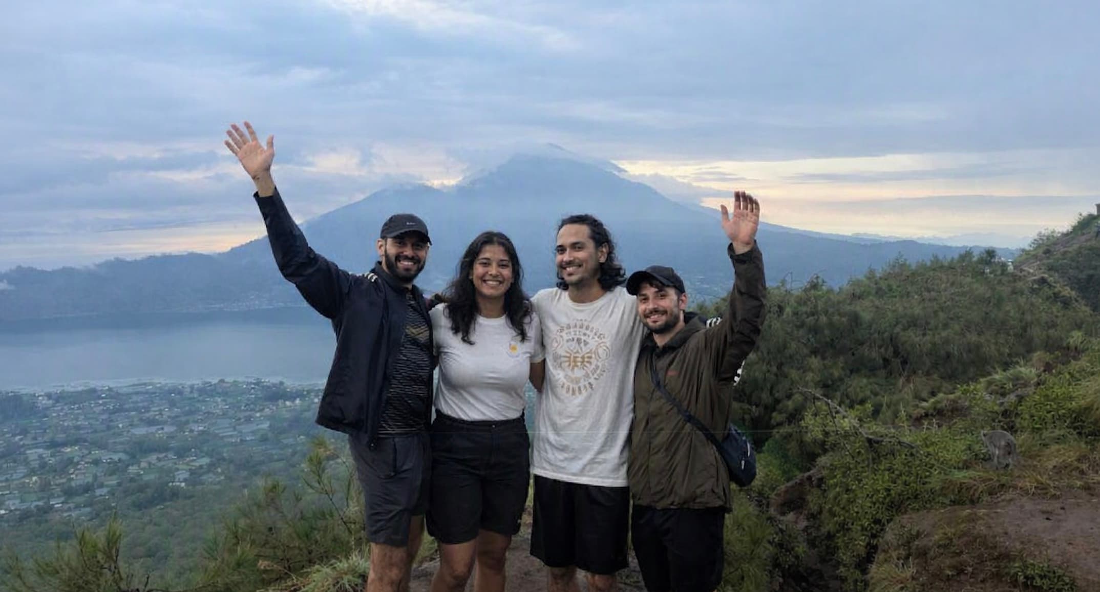 Four interns waving at the summit of Mount Batur with the crater lake behind them