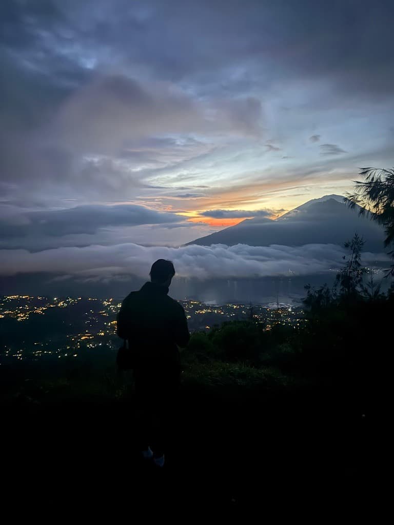 A student silhouetted against sunrise breaking over a sea of cloud below the summit